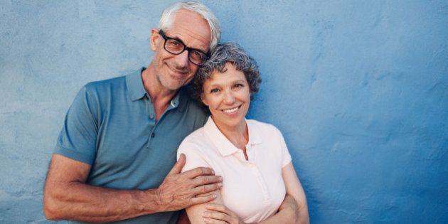 Portrait of smiling mature couple standing together against blue background. Happy middle aged man and woman against a wall.