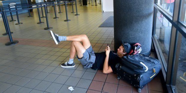 Traveller Santiago Aldrete, who arrived from Bali and is awaiting his flight to Mexico City, gets comfortable on the ground while charging his phone at Los Angeles International Airport on July 1, 2016 where a record 1.207 million people are expected to pass through during their travels over the Fourth of July weekend. LAX officials said the number of travelers anticipated to use the airport is up 9.7 percent from last year's record 1.1 million people over the holiday travel period, which runs from today through Tuesday July 5. / AFP / Frederic J. BROWN (Photo credit should read FREDERIC J. BROWN/AFP/Getty Images)