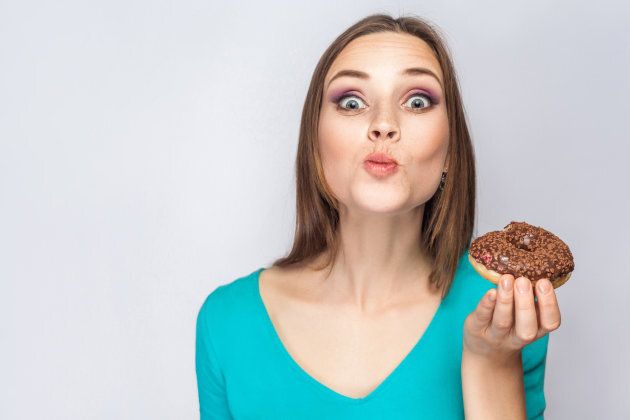 Portrait of beautiful girl with chocolate donuts. eating and looking at camera with funny face. studio shot on light gray background.