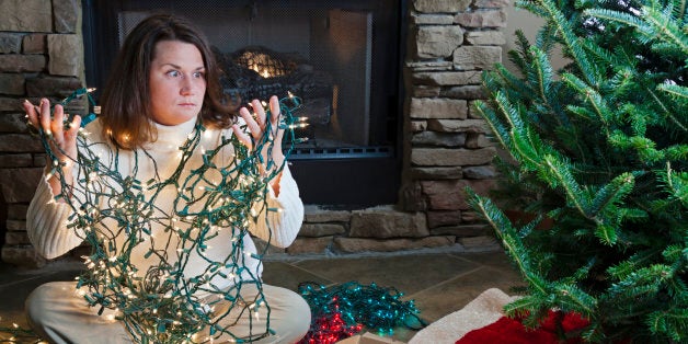 Young woman sitting next to Christmas tree holding entangled string of lights