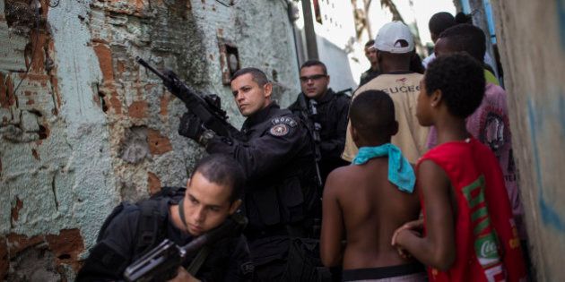 Special Operations Battalion (BOPE) Police officers patrol as residents move about the Sao Carlos slum complex where the bodies of two men were found in Rio de Janeiro, Brazil, Friday, May 15, 2015. The bodies of two young men were discovered late Thursday in this so-called