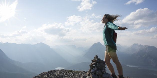 Young woman stands on summit, arms outstretched