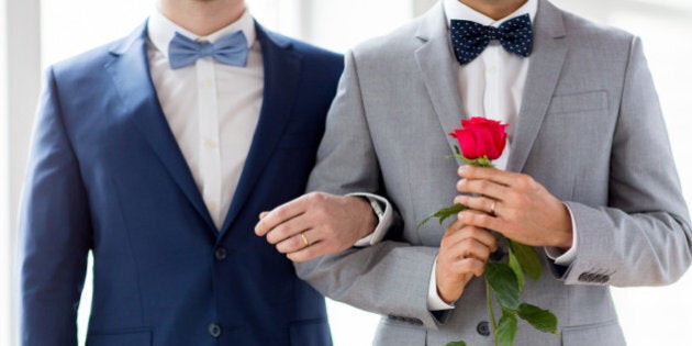 people, homosexuality, same-sex marriage and love concept - close up of happy male gay couple with red rose flower holding hands on wedding