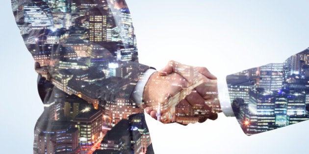 Double exposure of two business men shaking hands with a city view of the financial district at night.