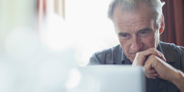 Senior man with hands clasped using laptop