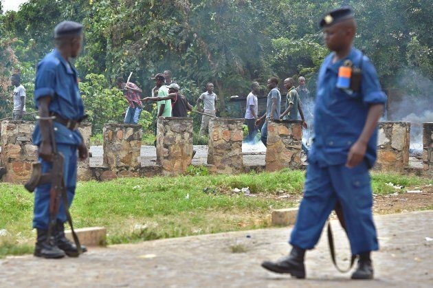 Burundian police look on as members of the Imbonerakure, armed with sticks, destroy barricades erected by protestors opposed to the Burundian President's third term. The Imbonerakure have been allowed to operate largely with impunity by the Burundian government.