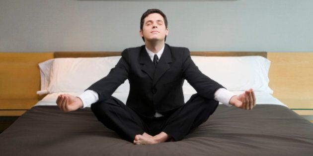 Businessman meditating on the bed in a hotel room