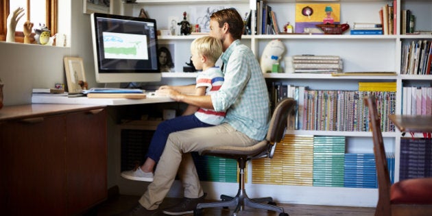 Boy sitting on father's lap at computer desk in living room