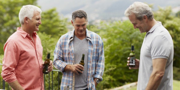 Happy mature male friends having beer while looking at barbecue in yard