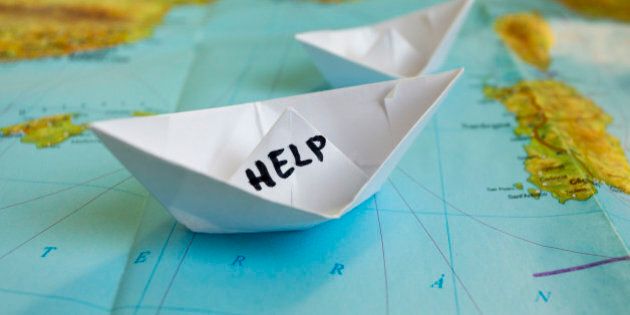 White paper boat onto world map with 'Help' sign on it.