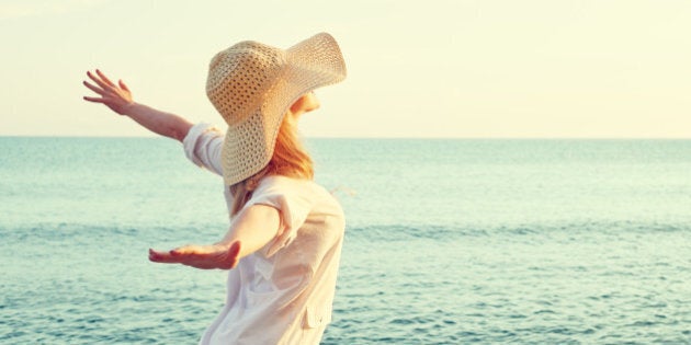 Happy beauty woman in hat is back opened his hands, relaxes and enjoys the sunset over the sea on the beach