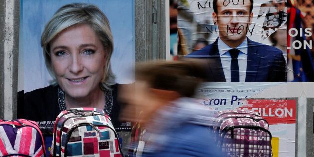 A woman walks past official posters of candidates for the 2017 French presidential election Marine Le Pen, French National Front (FN) political party leader (L) and Emmanuel Macron, head of the political movement En Marche !, or Onwards !, (R) on a local market in Bethune, France April 24, 2017. REUTERS/Pascal Rossignol