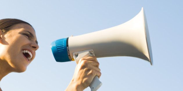 Woman shouting into megaphone, low angle view, cropped