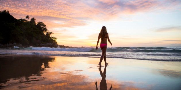 A woman walking in the sand on a tropical beach at sunset.