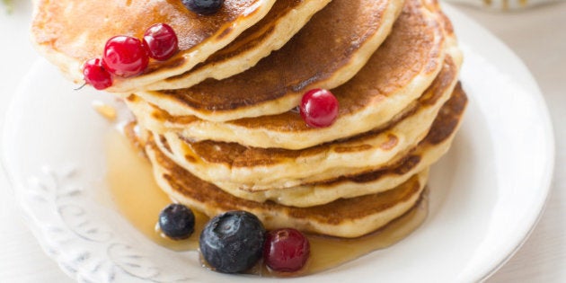 Stack of pancakes topped with blueberries, cranberries and honey on white plate on white table. Vertical breakfast image