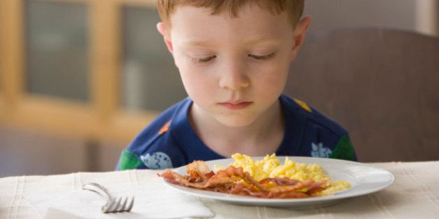Caucasian boy looking at plate of eggs and bacon