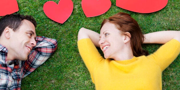 Couple laying in grass,surrounded by hearts.