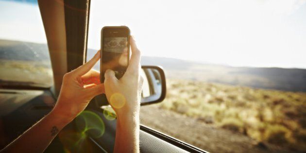 Woman riding in front seat of car driving through desert taking digital photo with smartphone