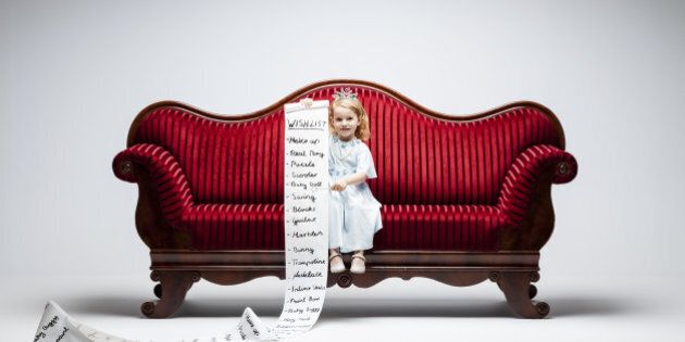 3 year princess girl sitting on red vintage sofa and holding an extraordinary long list of material whishes.