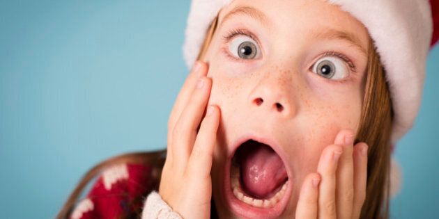 Color image of a little girl with a stressed/shocked/surprised look on her face. She is wearing a Santa hat and an ugly Christmas sweater.