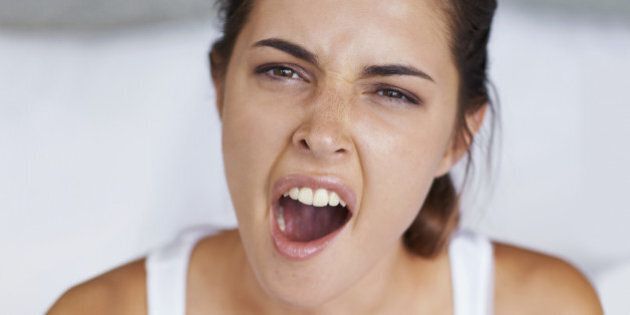 Shot of a young woman giving a big yawn while sitting with a cup of coffee in bed