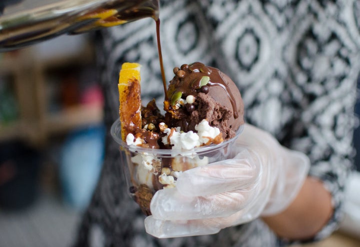 Sen serving up a breakfast ice cream cup topped with popcorn, granola, seeds, an orange segment, chocolate syrup and coffee. No words.