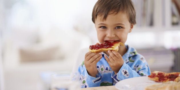 A cute little boy eating toast with jam