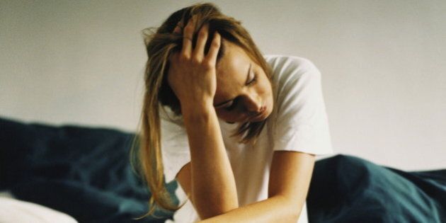 Young woman sitting on edge of bed, holding head in hand