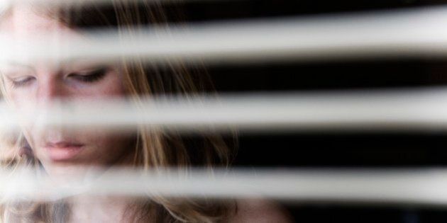 Portrait of a young woman as seen through open blinds.