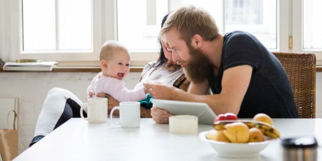 Young mother and father with newborn baby sitting in their kitchen and having fun together
