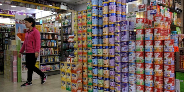 In this Friday, April 10, 2015 photo, a woman walks past cans of baby formula stacked in a shop at a district regarded as a hub of