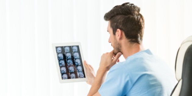 Male doctor studying an MRI scan of the brain on digital tablet. Actual scan of the young man's brain after the brain tumor removal.