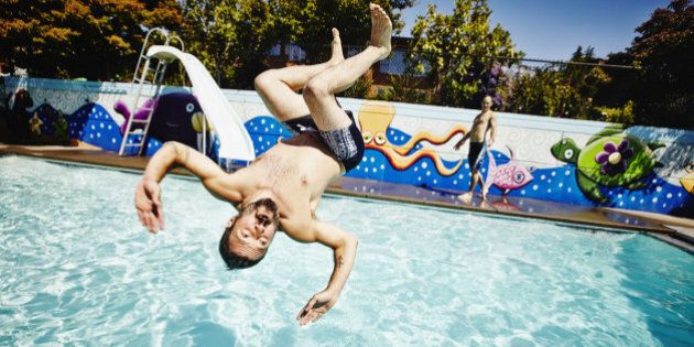 Man doing backflip into outdoor swimming pool on summer afternoon with friend watching in background
