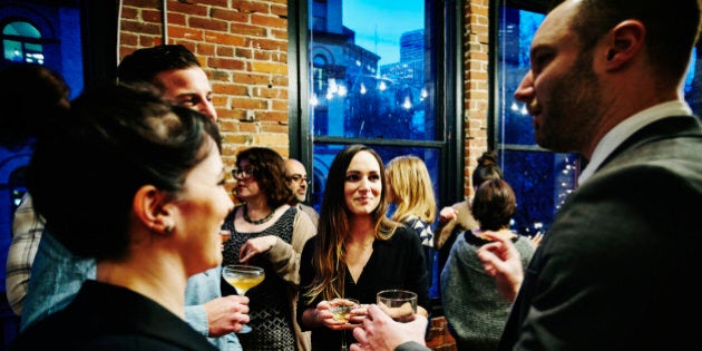 Group of friends laughing and having drinks together during dinner party in loft apartment