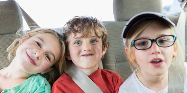 Caucasian children smiling in back seat of car