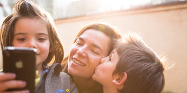 Mother with kids taking photos with smartphone in funny moment and sunset light.