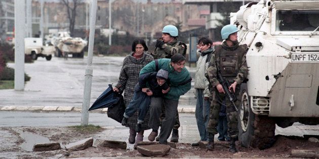 The residents of Sarajevo take cover from sniper fire behind a United Nations Protection Force (UNPROFOR) armoured vehicle in 1993.