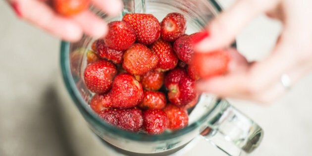 Fresh strawberries putting in blender cup and hands with some berries are blurry.