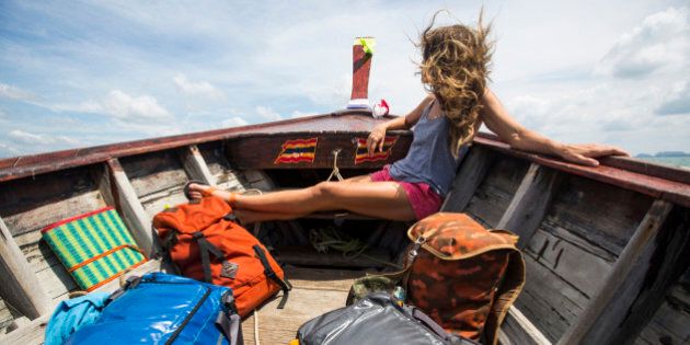 A woman with multiple bags traveling on a long-tail boat in Thailand.
