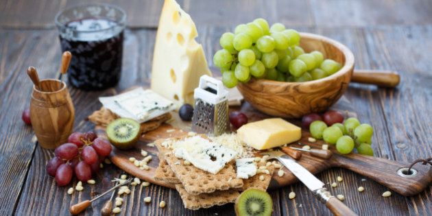 Breakfast with crackers, blue cheese, grape, kiwi, nuts and glass of wine on old rustic board with knife and stickers lying around