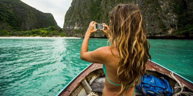 A woman taking a photo while riding on a long tail boat to a tropical island in Thailand.