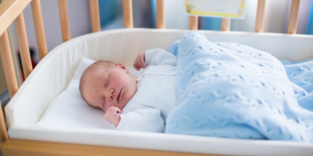 Newborn baby in hospital room. New born child in wooden co-sleeper crib. Infant sleeping in bedside bassinet. Safe co-sleeping in a bed side cot. Little boy taking a nap under knitted blanket.