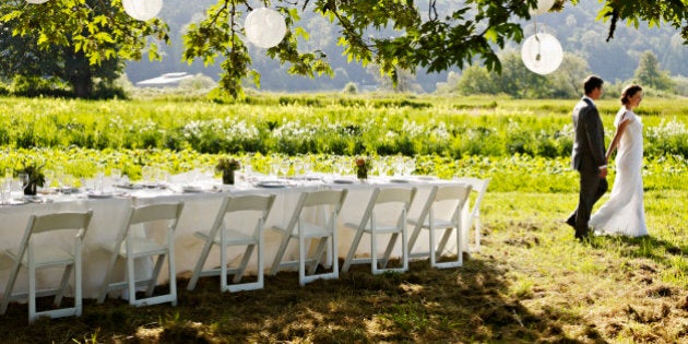 Bride and groom holding hands walking past banquet table under tree in field