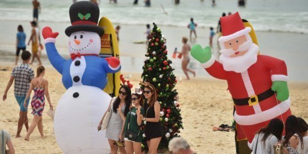 Visitors take photos in front of an inflatable snow man and Santa Claus on Bondi Beach on Christmas Day, December 25, 2014. Bondi Beach is a popular destination for tourists on Christmas Day. AFP PHOTO/Peter PARKS (Photo credit should read PETER PARKS/AFP/Getty Images)