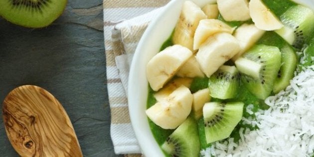 Green smoothie bowl with spinach, fresh kiwi fruit, bananas and coconut on a slate background