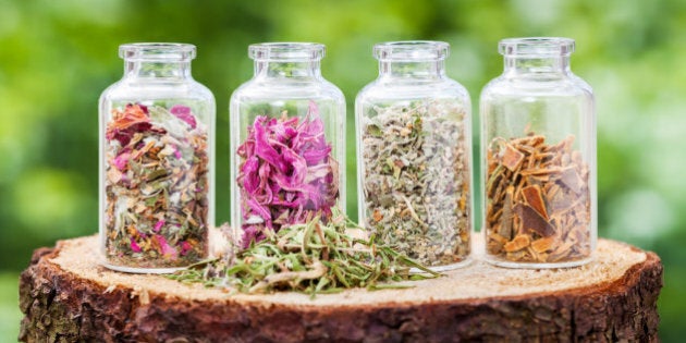 Glass bottles with healing herbs on wooden stump on green background, herbal medicine.