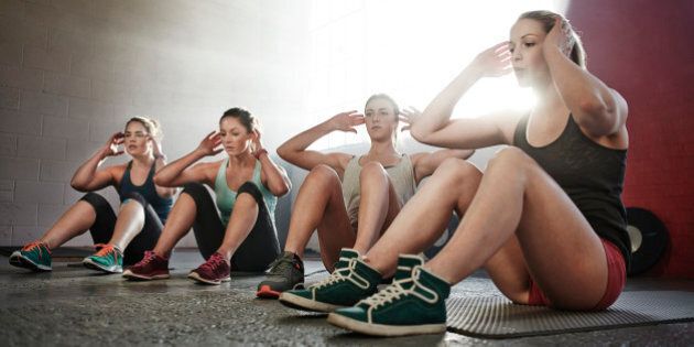 Four young women fitness training, doing sit-ups together in urban industrial gym.