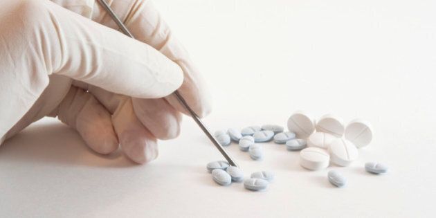 'White latex gloved hand holding, counting and preparing medicinal prescription blue and white pills isolated on white background.'