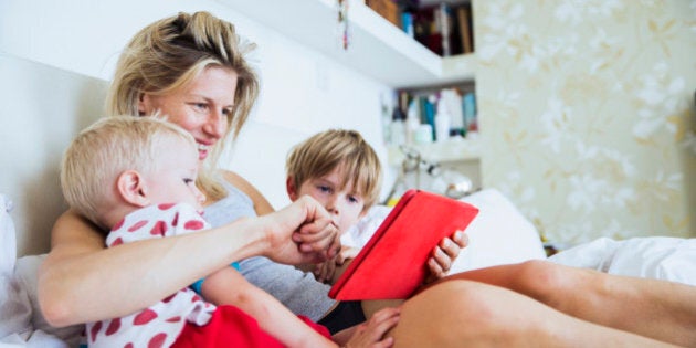 Mother with her sons watching tablet in bed