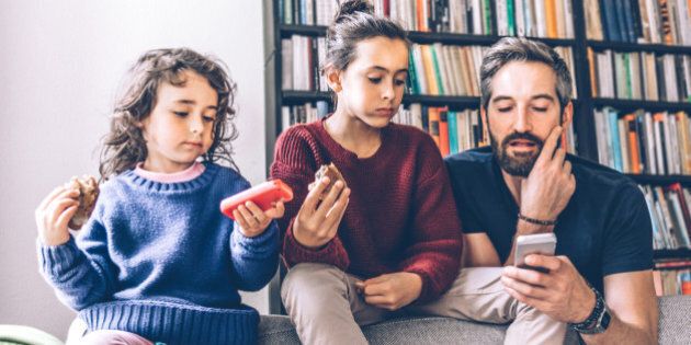 bearded father and two daughters on sofa looking together at mobiles